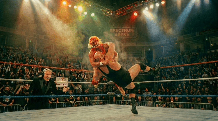 Wrestler in blue tights kicking opponent wearing black trunks in a crowded wrestling ring