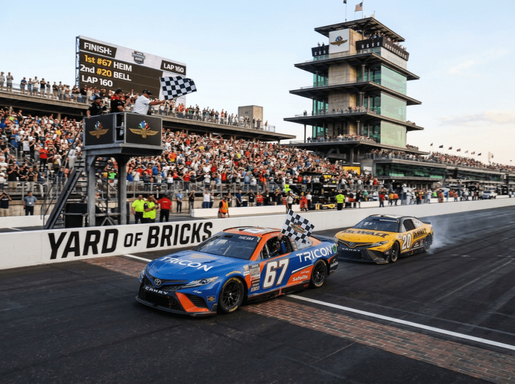 Race truck number 67 leads truck number 20 at Brickyard 400 start/finish line as checkered flag is waved